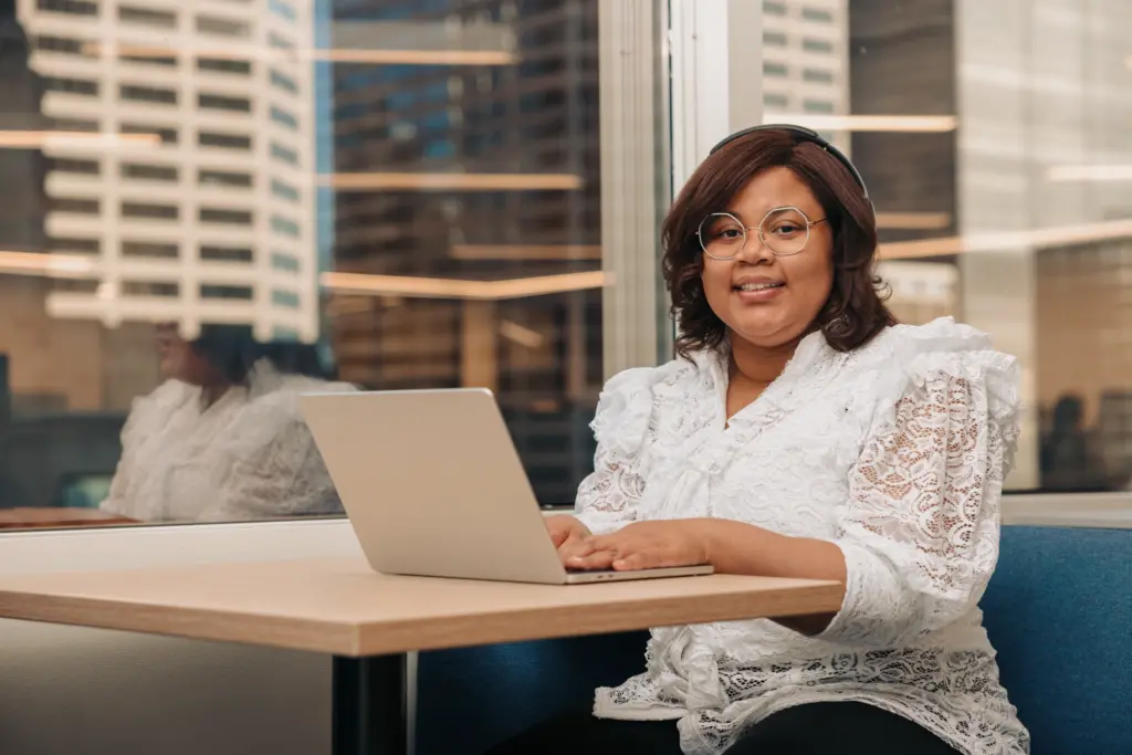 A young woman with a developmental disability works on a laptop in an office. Behind her, a window reveals a cityscape.